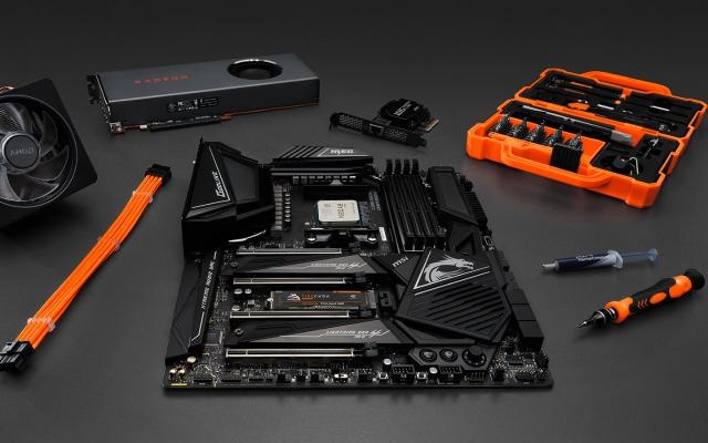 Real gaming PC components displayed separately on a desk, including GPU, CPU, RAM, SSD, motherboard, PSU, cooler, and PC case.