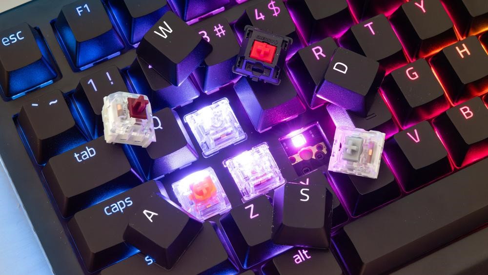 Collection of RGB mechanical gaming keyboards with different switch types visible on a modern gaming desk setup